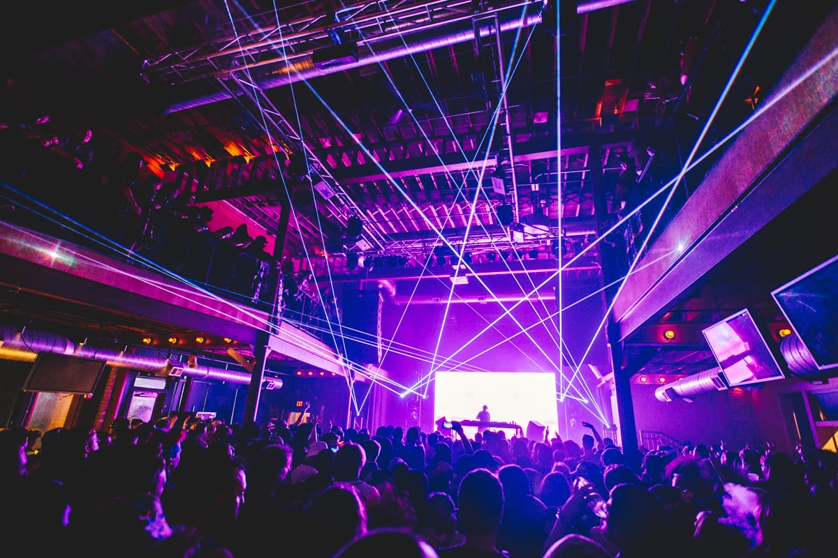 A DJ performing on stage in a hall in front of a large crowd